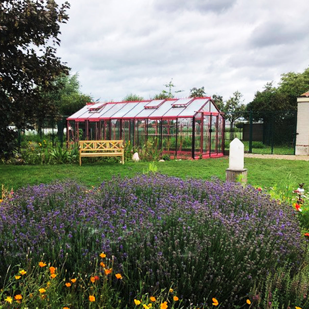 Vaxthusbolaget_vaxthus_R310_rött i en parkliknande trädgård med blommor i förgrunden